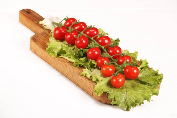 Созревший свежий органический бранч помидоров черри на разделочной доске с зеленым салатом на белом столе — стоковое фото