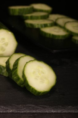 Siyah kesme tahtası ve ahşap rustik arka plan taze dilimlenmiş salatalık. Masada yeşil salatalık Düz yatıyordu desen