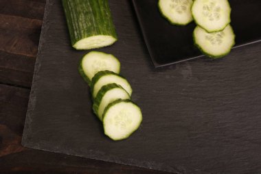 Siyah kesme tahtası ve ahşap rustik arka plan taze dilimlenmiş salatalık. Masada yeşil salatalık Düz yatıyordu desen. Üstte görüntü