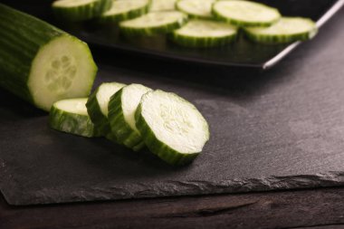 Siyah kesme tahtası ve ahşap rustik arka plan taze dilimlenmiş salatalık. Masada yeşil salatalık Düz yatıyordu desen