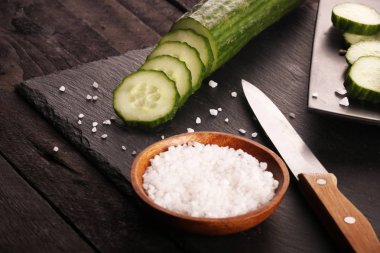 Siyah plaka ve siyah ahşap rustik masa üzerinde bıçak ve tuz ile dilimlenmiş yeşil salatalık.