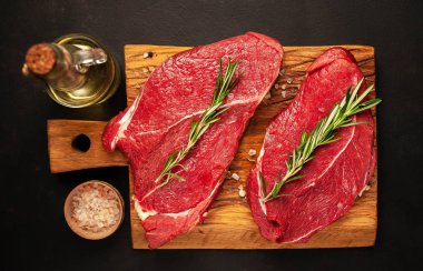 iki büyük ham New York biftek ile malzemeyi doğrama tahtası. karanlık taş arka plan üzerinde. 