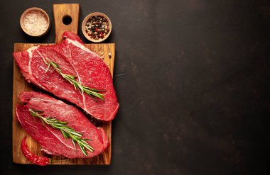 iki büyük ham New York biftek ile malzemeyi doğrama tahtası. arka planda karanlık taş. kopya alanı ile