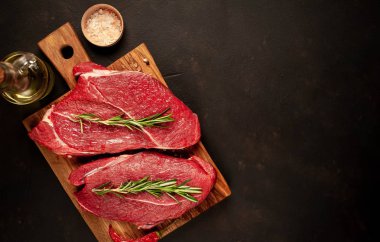 iki büyük ham New York biftek ile malzemeyi doğrama tahtası. arka planda karanlık taş. kopya alanı ile