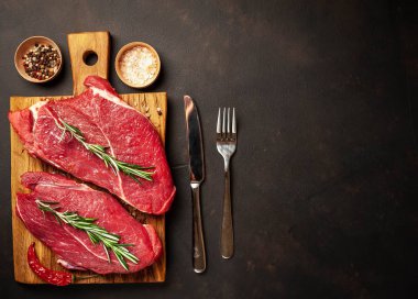 iki büyük ham New York biftek ile malzemeyi doğrama tahtası. arka planda karanlık taş. kopya alanı ile