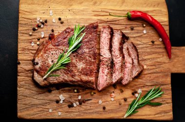 Bir kesme tahtası üzerinde malzemelerle New York siyah angus biftek yemeye hazır. Karanlık bir taş zemin üzerine akşam yemeğine hazır yemek.