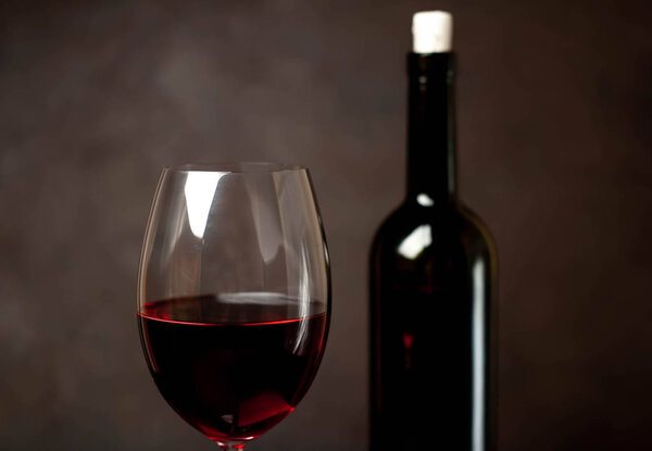 Wine glass with red wine and bottle against a stone background. 