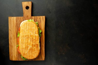 Grilled panini sandwich on wooden chopping board on stone background clipart