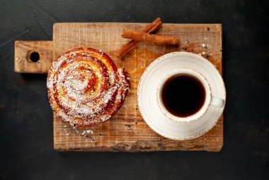 Taş arka planda ahşap doğrama tahtasında kahve ve tarçın kabuğu ile taze Cinnabon
