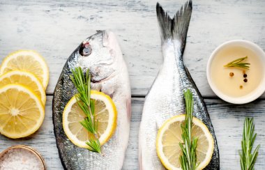 Eski ahşap arka planda limon dilimleri ve biberiye ile ham taze deniz bas