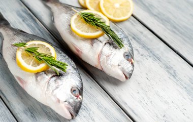 Eski ahşap arka planda limon dilimleri ve biberiye ile ham taze deniz bas