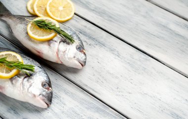 Eski ahşap arka planda limon dilimleri ve biberiye ile ham taze deniz bas