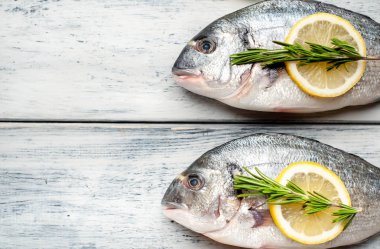 Eski ahşap arka planda limon dilimleri ve biberiye ile ham taze deniz bas