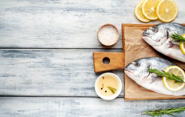 Eski ahşap arka planda limon dilimleri ve biberiye ile ham taze deniz bas