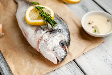 Eski ahşap arka planda limon dilimleri ve biberiye ile ham taze deniz bas