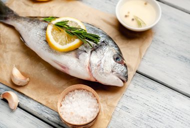 Eski ahşap arka planda limon dilimleri ve biberiye ile ham taze deniz bas