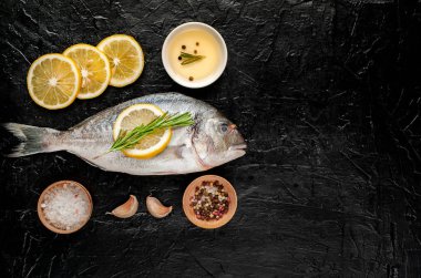 Çiğ deniz bas biberiye dalları, limon dilimleri ve taş arka planda baharatlar ile servis 