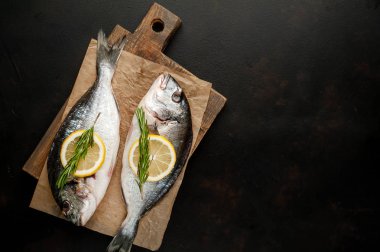 Taş arka planda limon dilimleri ve biberiye ile ham taze deniz bas 