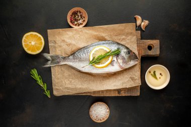 Çiğ deniz bas biberiye dalları, limon dilimleri ve taş arka plan üzerinde ahşap tahta üzerinde baharatlar ile servis 