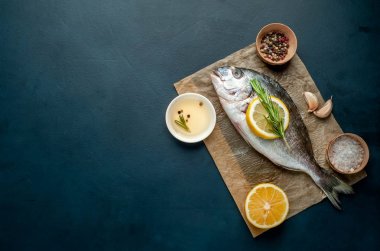 Çiğ deniz bas biberiye dalları, limon dilimleri ve taş arka planda kahverengi kağıt üzerinde baharatlar ile servis 