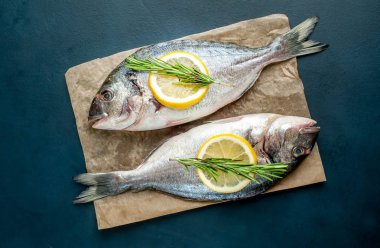 Taş arka planda limon dilimleri ve biberiye ile ham taze deniz bas 