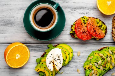 ahşap arka planda dilimlenmiş avokado, yumurta ve greyfurt ile tost ile servis edilen kahve fincan