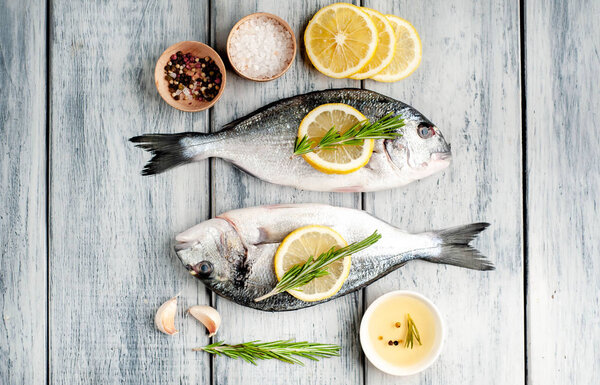 Сырой морской окунь подается с розмарином, ломтиками лимона и специями на деревянном фоне
 