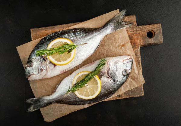 Taş arka planda limon dilimleri ve biberiye ile ham taze deniz bas 