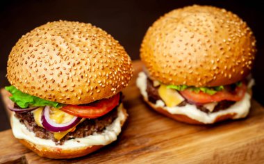 Koyu taş arka planda ahşap doğrama tahtasında taze ev yapımı Hamburgerler