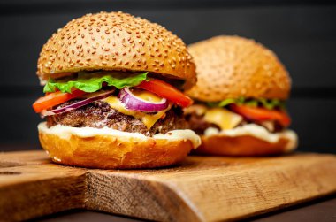 Koyu taş arka planda ahşap doğrama tahtasında taze ev yapımı Hamburgerler