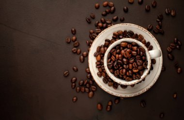 Kahverengi taş arka planda kavrulmuş kahve çekirdekleri dolu seramik fincan ve tencere 