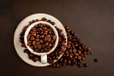 Kahverengi taş arka planda kavrulmuş kahve çekirdekleri dolu seramik fincan ve tencere 