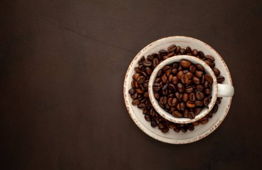 Kahverengi taş arka planda kavrulmuş kahve çekirdekleri dolu seramik fincan ve tencere 