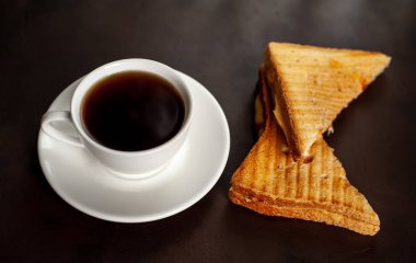 Siyah taş arka planda bir fincan kahve ile servis edilen ızgara sandviçler