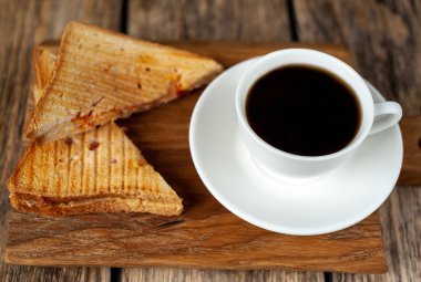 Ahşap arka planda bir fincan kahve ile servis edilen ızgara sandviçler