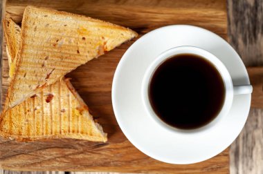 Close view of grilled sandwiches served with cup of coffee on wooden chopping board