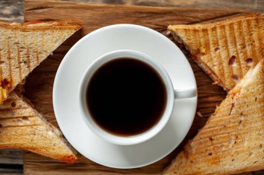 Close view of grilled sandwiches served with cup of coffee on wooden chopping board