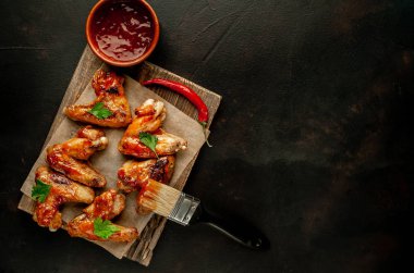 Siyah taş arka planda kesme tahtasında maydanoz ile barbekü sosu ızgara tavuk kanatları