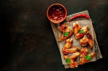 Siyah taş arka planda kesme tahtasında maydanoz ile barbekü sosu ızgara tavuk kanatları