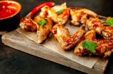 Siyah taş arka planda kesme tahtasında maydanoz ile barbekü sosu ızgara tavuk kanatları