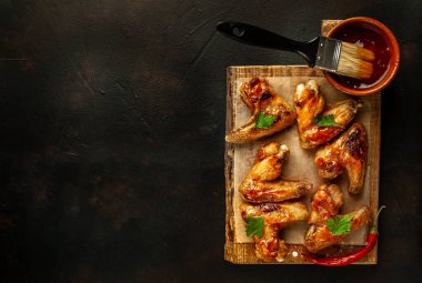 Siyah taş arka planda kesme tahtasında maydanoz ile barbekü sosu ızgara tavuk kanatları