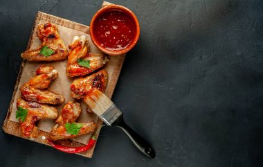 Siyah taş arka planda kesme tahtasında maydanoz ile barbekü sosu ızgara tavuk kanatları