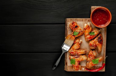 Siyah ahşap arka planda kesme tahtasında maydanoz ile barbekü sosu ızgara tavuk kanatları