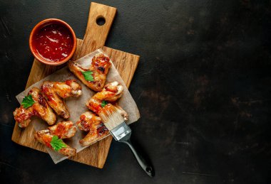 Siyah taş arka planda kesme tahtasında maydanoz ile barbekü sosu ızgara tavuk kanatları