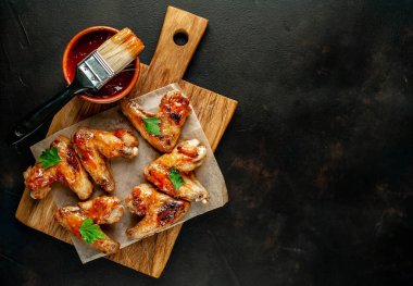 Siyah taş arka planda kesme tahtasında maydanoz ile barbekü sosu ızgara tavuk kanatları