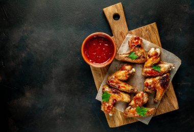 Siyah taş arka planda kesme tahtasında maydanoz ile barbekü sosu ızgara tavuk kanatları