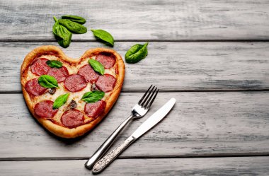 ahşap arka plan üzerinde salam ve taze fesleğen yaprakları ile peynir kalp pizza