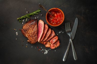 Dilimlenmiş taze sığır eti biftek taş arka plan üzerinde domates sosu ve biberiye dal ile servis