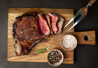 Siyah taş arka plan üzerinde ahşap doğrama tahtası üzerinde baharat ile Yağlı ızgara domuz biftek