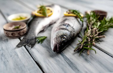 Gri ahşap arka plan üzerinde limon dilimleri ve biberiye dalları ile çiğ balık